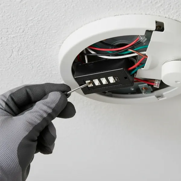 electrician adjusting dip switches on a ceiling fan receiver inside canopy for pairing