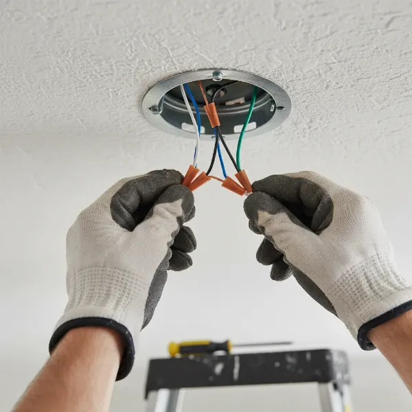 Hands connecting ceiling fan wires with wire nuts inside an electrical box.